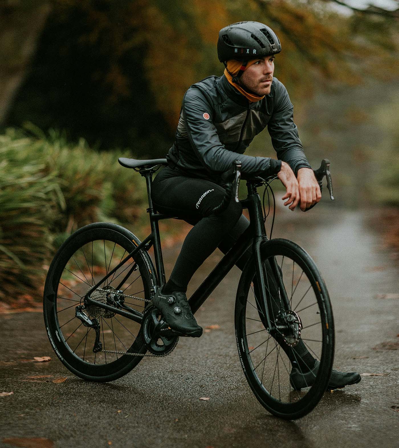 A man wearing a helmet and biking gear resting on his bicycle along a tree-lined trail.