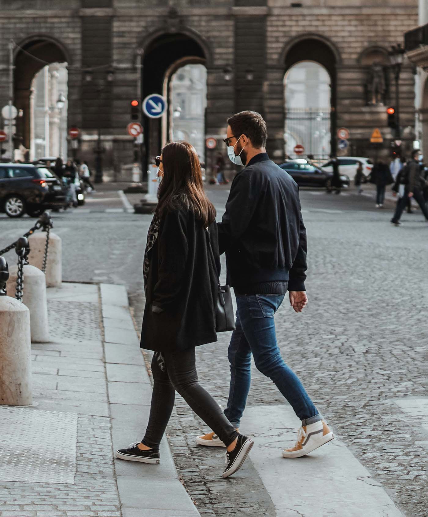 Man and woman crossing a cobblestone street at a city intersection, emphasizing safe pedestrian behavior in high-traffic urban areas.