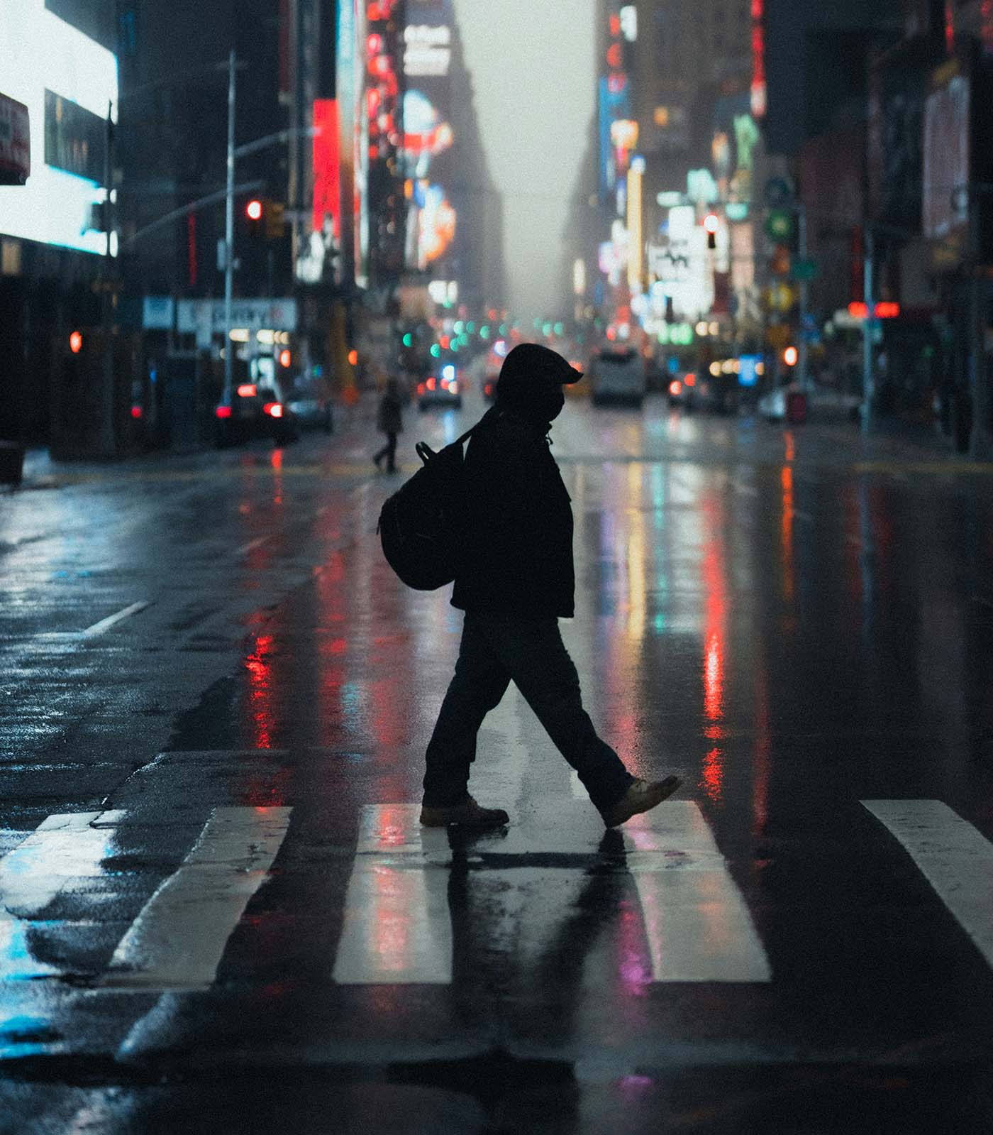 Silhouette of a pedestrian crossing a city street at night with blurred headlights and neon reflections, highlighting nighttime pedestrian accident risks.