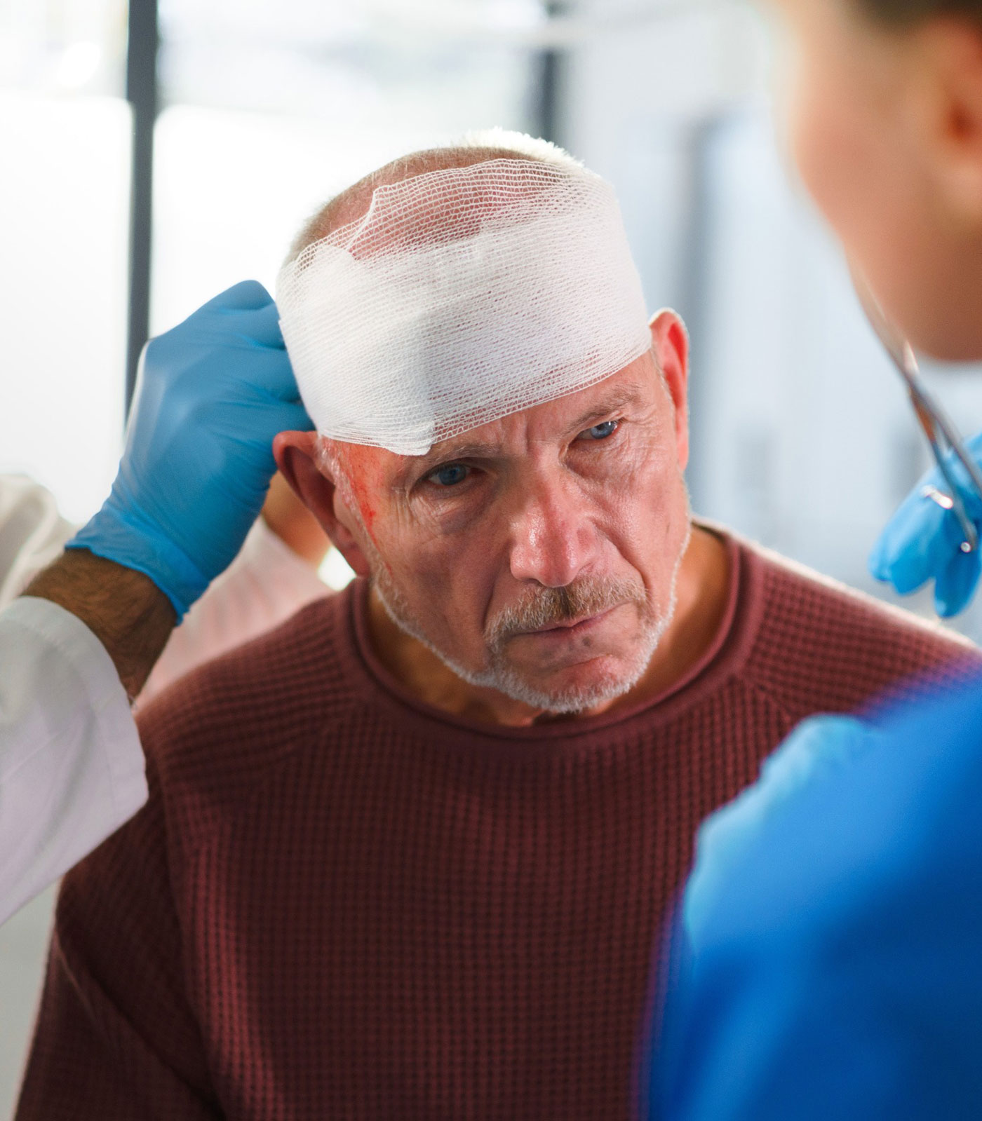 Older man with a head bandage receiving medical care from doctors after a possible brain injury.