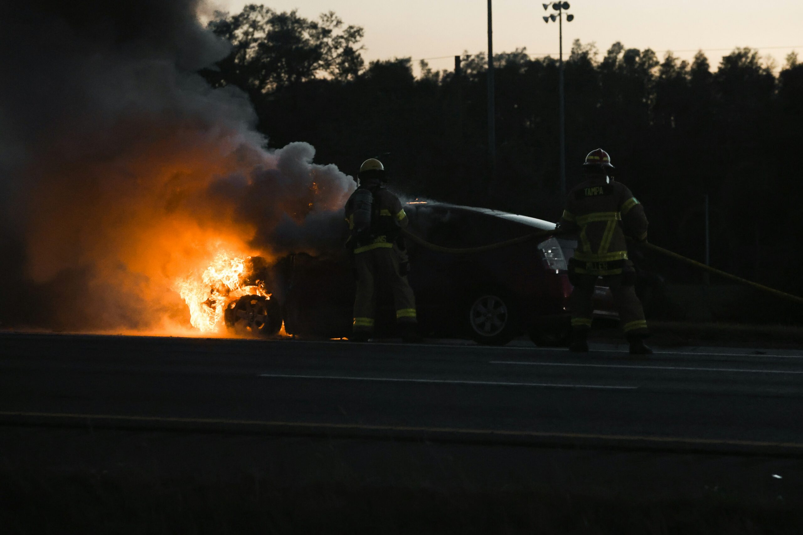 Firefighters extinguishing a burning vehicle on the highway after a serious car crash at dusk